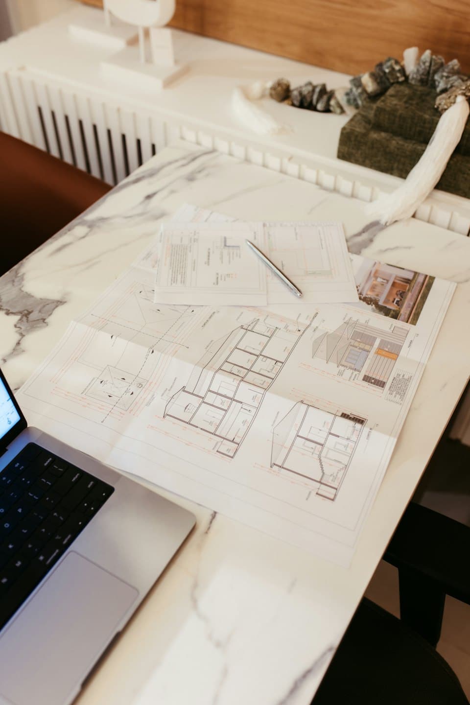 Plany architektoniczne i laptop na marmurowym stole.